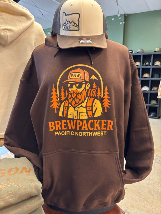 Chocolate brown hoodie featuring a bold orange and yellow graphic of a bearded backpacker surrounded by pine trees, with the text “Brewpacker – Pacific Northwest.”